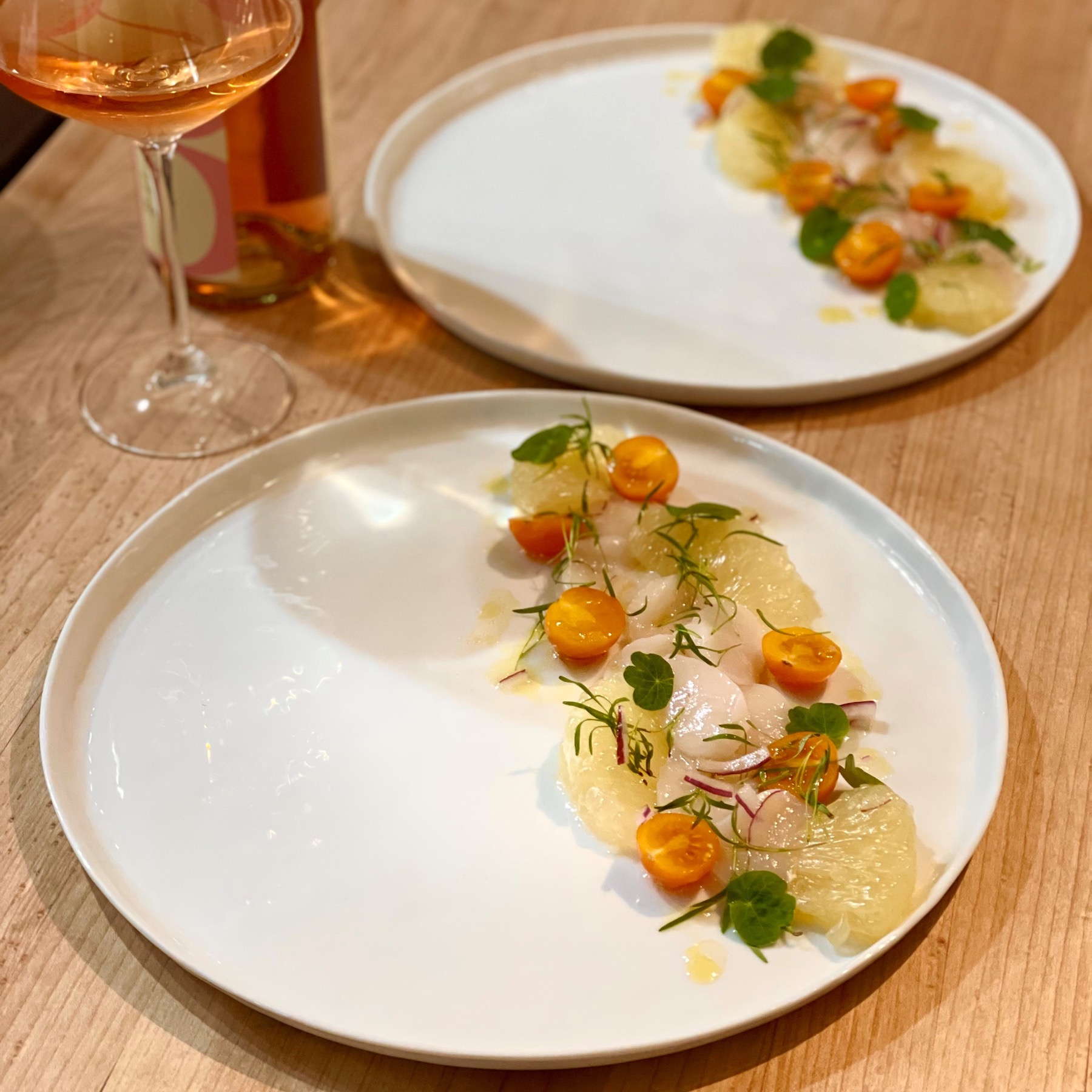 Sea scallop crudo plated with grapefruit, tomatoes, herbs, and vinaigrette